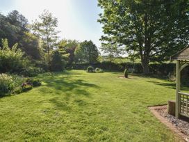 A garden with grass trees flowerbeds a swing and a gazebo at Lavender Cottage in Market Weighton