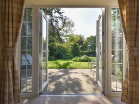 Open glass doors with plaid curtains leading to a patio and garden with chairs and trees at Lavender Cottage in Market Weighton