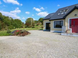 A gravel driveway leading to a yellow house with a red door and multiple windows with a flower bed to the side and trees in the background at Curraha in Lauragh County Kerry