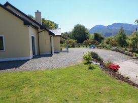 A yellow house with a gravel driveway and green lawn with flowers and trees with mountains in the background at Curraha in Lauragh County Kerry