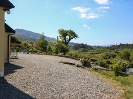 A gravel driveway beside a yellow house with a view of trees bushes and mountains at Curraha in Lauragh County Kerry