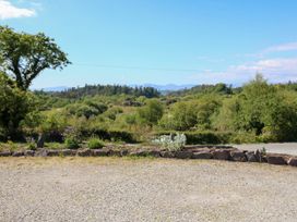 A gravel area with a rock border and plants with green hills and trees in the background at Curraha in Lauragh County Kerry
