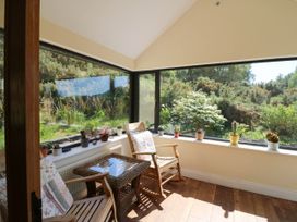 A sunroom with wooden rocking chairs and a wicker table surrounded by potted plants on the window ledge at Curraha in Lauragh County Kerry