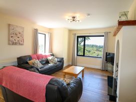 A living room with two black leather sofas a wooden coffee table and large windows showing greenery at Curraha in Lauragh County Kerry