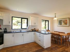 A kitchen with white cabinets black countertops a sink and a wooden dining table with chairs at Curraha in Lauragh County Kerry
