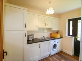 A kitchen with white cabinets a washing machine a sink a yellow basket a stereo and a black door window at Curraha in Lauragh County Kerry