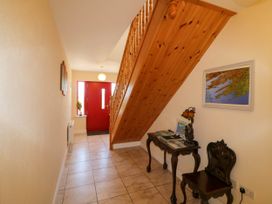 A hallway with a red door a wooden staircase a small table with a lamp and chair and a map on the wall at Curraha in Lauragh County Kerry