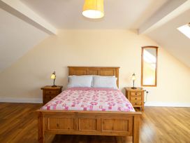 A bedroom with a wooden bed a pink quilt two bedside tables with lamps and a wall mirror at Curraha in Lauragh County Kerry