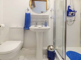 A bathroom with a toilet, pedestal sink with a round mirror above it, blue towel, blue soap dispenser, blue trash can, and a glass shower enclosure with a blue shower mat at Little Cow House in Pontfaen near Chirk