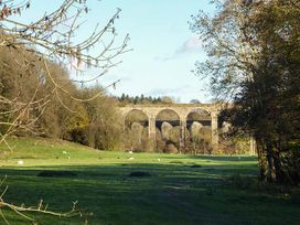 A grassy field with sheep and a stone arch bridge in the background at Little Cow House in Pontfaen near Chirk