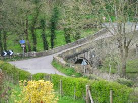 A rural scene with a stone bridge over a road and trees at Little Cow House in Pontfaen near Chirk