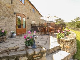 A stone patio with wooden table and chairs under an umbrella and potted flowers at Little Cow House in Pontfaen near Chirk