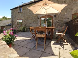A stone patio with wooden table and chairs under a large umbrella and potted flowers at Little Cow House in Pontfaen near Chirk