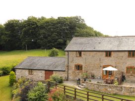 A stone building with a patio table and umbrella in a garden with trees and shrubs at Little Cow House in Pontfaen near Chirk