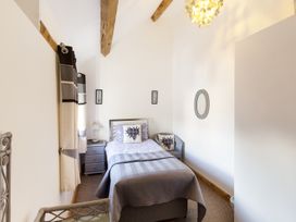 A bedroom with a single bed with gray bedspread and heart pillows a bedside table with lamp curtains a wicker chair and wooden beams on the ceiling at Little Cow House in Pontfaen near Chirk