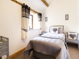 A bedroom with a single bed a gray quilt curtains a window a nightstand with a lamp a wicker chair and decorative cushions at Little Cow House Pontfaen near Chirk