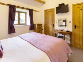 A bedroom with a bed covered in a pink quilt near a window with purple curtains two wooden doors a wooden chest of drawers a wall-mounted TV and a small wooden table with a mirror at Little Cow House in Pontfaen near Chirk