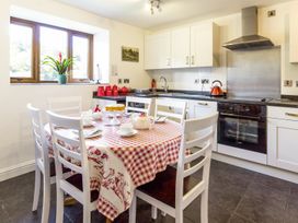 A kitchen with white chairs around a table covered with a red checkered tablecloth and kitchen cabinets with a stove and kettle at Little Cow House Pontfaen near Chirk