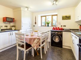 A kitchen with white cabinets a black washing machine a table with six white chairs and a red checkered tablecloth at Little Cow House Pontfaen near Chirk