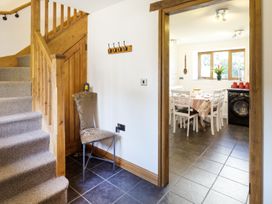 A stairway with carpeted steps and a wooden railing next to a chair and a doorway leading to a dining area with a table and chairs at Little Cow House Pontfaen near Chirk