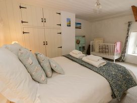 A bedroom with a bed, crib, and wardrobe at Fern Cottage in Aberporth