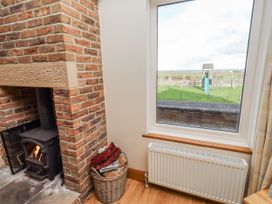 A living room with a fireplace and a view of a playground at Home Stead Cottage Embleton