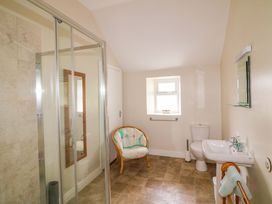 A bathroom with a shower, sink, toilet, and chair at Curradoon House in Touraneena, County Waterford