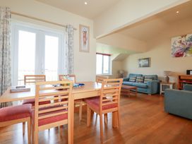 A dining area with wooden table and chairs next to a sitting area with blue sofas and paintings at The Beach House in Porth near Newquay