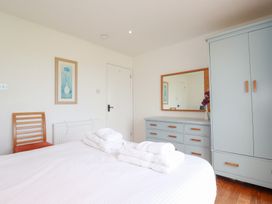 A bedroom with a bed, folded towels, a wooden chair, a wardrobe, a dresser with a mirror, and framed artwork at The Beach House in Porth near Newquay