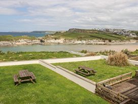 A garden with picnic benches overlooking a bay with cliffs and buildings at The Beach House in Porth near Newquay