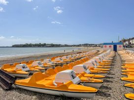 Rows of yellow and white pedal boats lined up on a pebble beach near the sea with a town in the background at Casterbridge Upwey near Weymouth