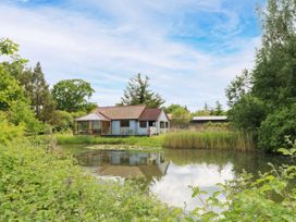 A house near a pond with trees and grass at Dragonfly Lodge Whinburgh near Dereham