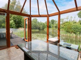 A conservatory with a glass table and view of water at Dragonfly Lodge Whinburgh near Dereham