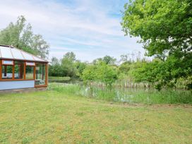 A garden area with a pond and a conservatory at Dragonfly Lodge in Whinburgh near Dereham