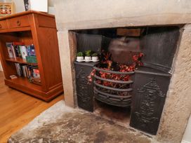 An old fireplace with decorative black metal panels and red leaves inside next to a wooden bookshelf with books and games at Quoits Cottage in Beck Hole near Goathland