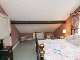 A bedroom with a double bed with floral bedding and towels on it a wooden floor a bedside table with a lamp and a chair with cushions at Quoits Cottage in Beck Hole near Goathland