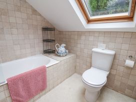 A bathroom with a bathtub with a pink towel a toilet and a window on a slanted ceiling at Quoits Cottage in Beck Hole near Goathland