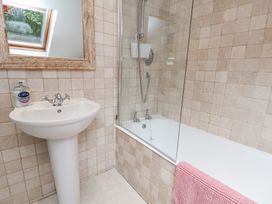 A bathroom with a pedestal sink, a mirror, a bathtub with shower, and a pink towel at Quoits Cottage in Beck Hole near Goathland