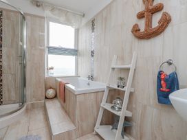 A bathroom with a bathtub, shower, and shelving at The View in Criccieth