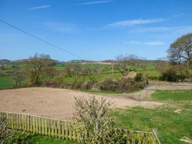 An outdoor rural area with green fields trees and a fenced sandy patch at Ysgubor - Barn in Betws Yn Rhos