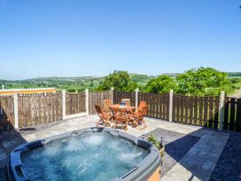 An outdoor patio with a hot tub and a wooden table with chairs surrounded by a wooden fence and greenery at Ysgubor - Barn in Betws Yn Rhos