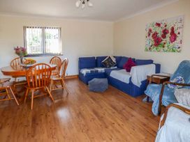 A living room with a wooden dining table and chairs blue sofas armchairs and a floral painting on the wall at Ysgubor - Barn in Betws Yn Rhos