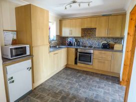 A kitchen with wooden cabinets a microwave a built-in oven a sink and a tiled backsplash at Ysgubor - Barn in Betws Yn Rhos