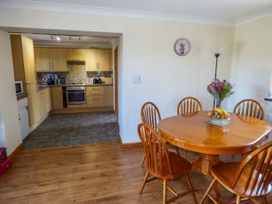 A dining area with a wooden table and six chairs next to a kitchen with wooden cabinets and tiled floor at Ysgubor - Barn in Betws Yn Rhos