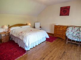 A bedroom with a double bed two bedside tables with lamps a wooden dresser a chair and a floral cushioned chair at Ysgubor - Barn in Betws Yn Rhos