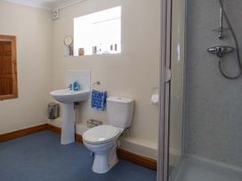 A bathroom with a toilet, pedestal sink, towel holder with a blue towel, shower enclosure, and small window at Ysgubor - Barn in Betws Yn Rhos