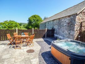 An outdoor patio with a wooden table and chairs and a hot tub next to a stone building at Ysgubor - Barn in Betws Yn Rhos
