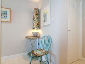 A corner with a small round table, a decorative lamp, a worn turquoise wooden chair, and framed pictures on the walls at St Tudwals View in Abersoch