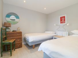 A bedroom with two single beds a wooden chest of drawers a green chair and wall decorations at St Tudwals View in Abersoch