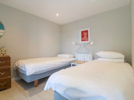 A bedroom with two single beds a wooden chest of drawers and a nightstand with two lamps at St Tudwals View in Abersoch